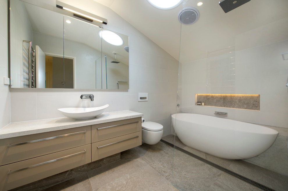 メルボルンにある中くらいなモダンスタイルのおしゃれな浴室 (ベッセル式洗面器、ベージュのキャビネット、置き型浴槽、オープン型シャワー、壁掛け式トイレ、ベージュの壁、磁器タイルの床) の写真
