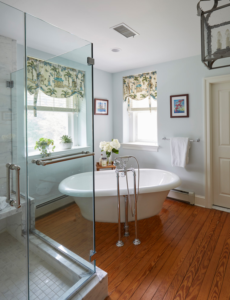 Design ideas for a large traditional ensuite bathroom in Philadelphia with beaded cabinets, medium wood cabinets, a freestanding bath, a double shower, a two-piece toilet, white tiles, marble tiles, grey walls, medium hardwood flooring, a submerged sink, marble worktops, brown floors and a hinged door.