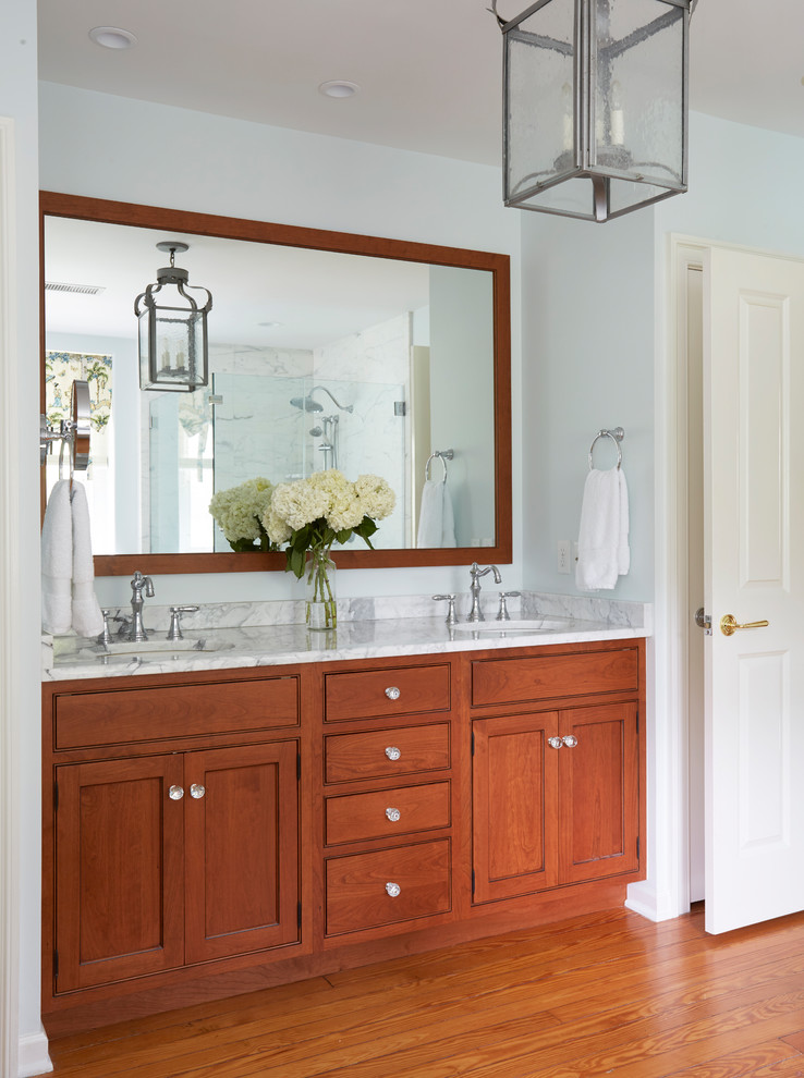 Photo of a large classic ensuite bathroom in Philadelphia with beaded cabinets, medium wood cabinets, a freestanding bath, a double shower, a two-piece toilet, white tiles, marble tiles, grey walls, medium hardwood flooring, a submerged sink, marble worktops, brown floors and a hinged door.