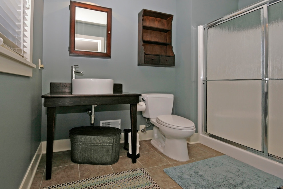 This is an example of a contemporary bathroom in Grand Rapids with freestanding cabinets, a two-piece toilet, grey walls, porcelain flooring, a vessel sink and wooden worktops.
