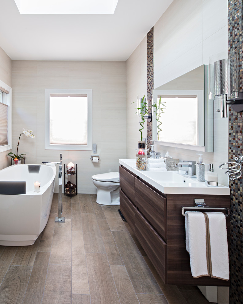 Aménagement d'une salle de bain principale contemporaine en bois foncé avec un placard à porte plane, une baignoire indépendante, un carrelage beige, un carrelage multicolore, un mur beige, parquet clair et un lavabo intégré.