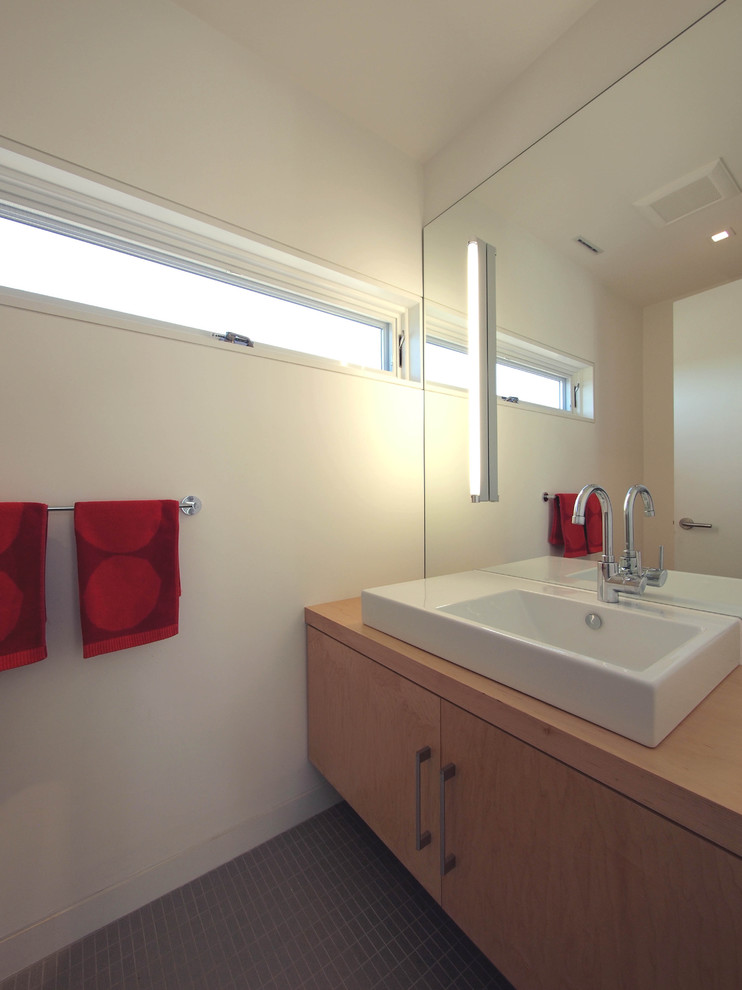 Example of a minimalist bathroom design in New York with flat-panel cabinets, light wood cabinets, wood countertops and an integrated sink