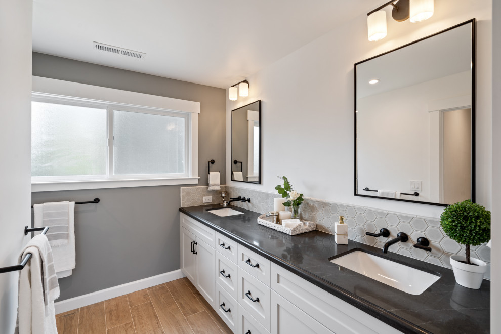 Exemple d'une salle de bain chic avec un placard à porte shaker, des portes de placard blanches, un carrelage gris, mosaïque, un mur blanc, un lavabo encastré, un sol marron, un plan de toilette noir, meuble double vasque et meuble-lavabo encastré.