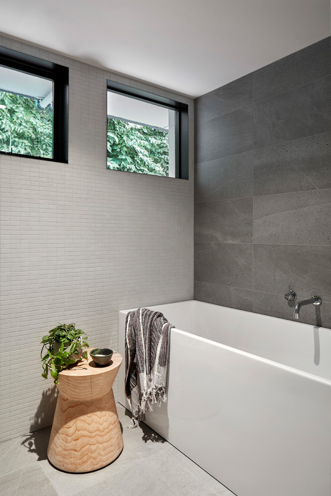 Modern inredning av ett litet vit vitt badrum för barn, med ett fristående badkar, grå kakel, grått golv, en dusch/badkar-kombination, en vägghängd toalettstol, keramikplattor, grå väggar, cementgolv, ett integrerad handfat, bänkskiva i akrylsten och med dusch som är öppen