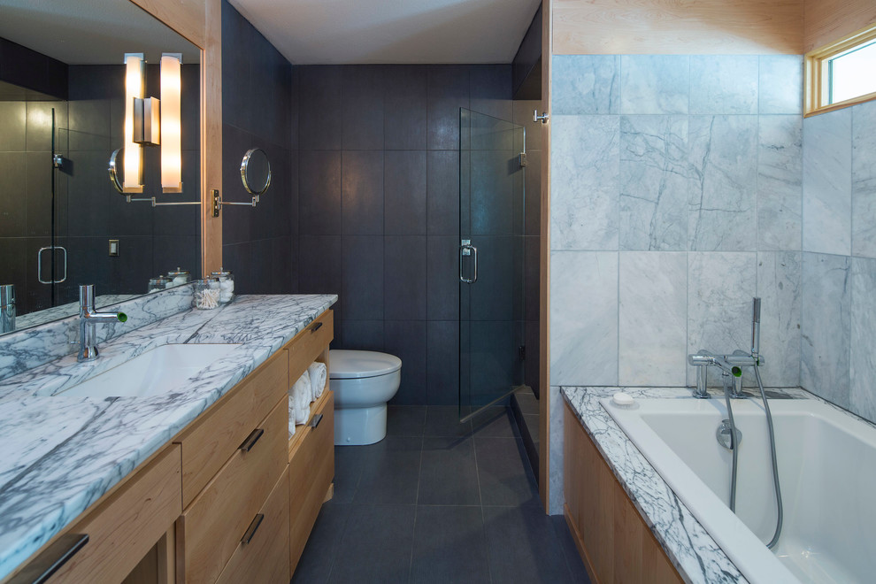Modern inredning av ett mellanstort en-suite badrum, med en dusch i en alkov, en toalettstol med hel cisternkåpa, grå kakel, porslinskakel, svarta väggar, klinkergolv i porslin, ett undermonterad handfat, släta luckor, skåp i ljust trä, ett platsbyggt badkar och marmorbänkskiva