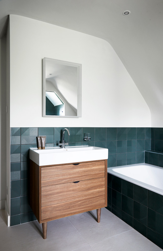 На фото: ванная комната в современном стиле с фасадами цвета дерева среднего тона, ванной в нише, зеленой плиткой, белыми стенами, консольной раковиной, серым полом и плоскими фасадами с