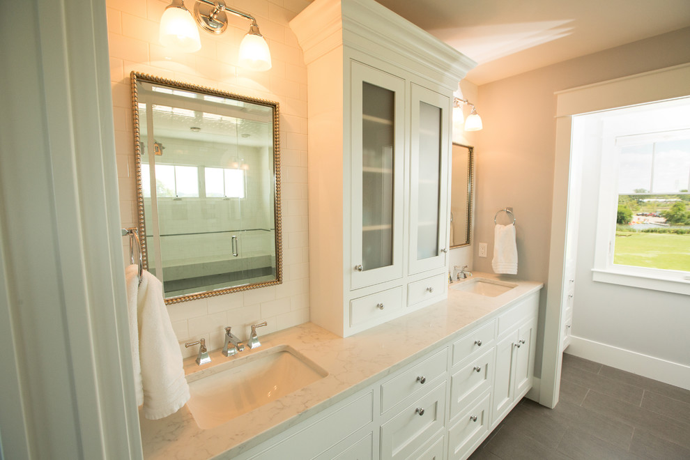 На фото: большая главная ванная комната в стиле неоклассика (современная классика) с фасадами в стиле шейкер, белыми фасадами, двойным душем, раздельным унитазом, белой плиткой, керамической плиткой, белыми стенами, полом из керамогранита, врезной раковиной, столешницей из искусственного кварца, серым полом и душем с распашными дверями