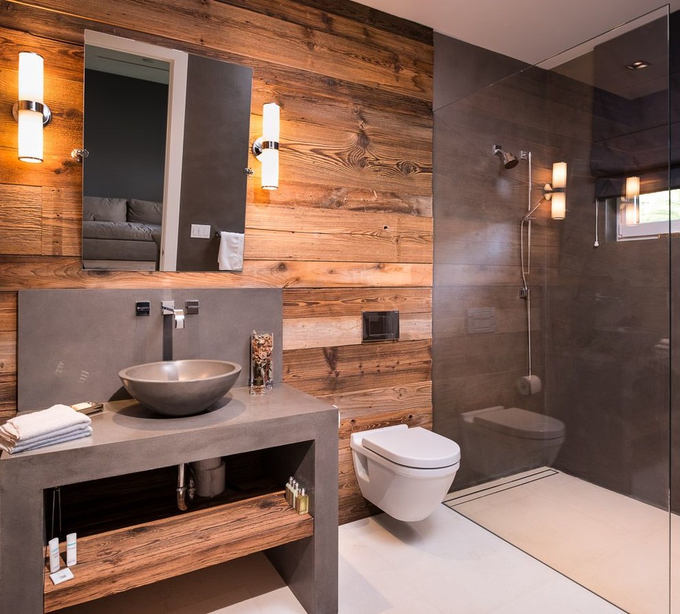 Mid-sized farmhouse limestone floor bathroom photo in Miami with a vessel sink, open cabinets, medium tone wood cabinets, concrete countertops, a wall-mount toilet and brown walls