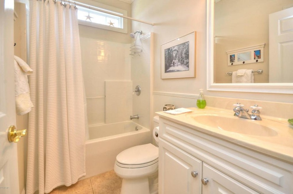 Inspiration for a small coastal shower room bathroom in Wilmington with white cabinets, granite worktops, raised-panel cabinets, an alcove bath, a shower/bath combination, a one-piece toilet, beige tiles, white walls, ceramic flooring, an integrated sink, beige floors and a shower curtain.