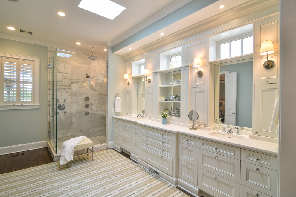 Klassisches Badezimmer En Suite mit Schrankfronten mit vertiefter Füllung, weißen Schränken, Eckdusche, grauen Fliesen, grüner Wandfarbe, dunklem Holzboden, Unterbauwaschbecken, braunem Boden, Falttür-Duschabtrennung und weißer Waschtischplatte in Charleston