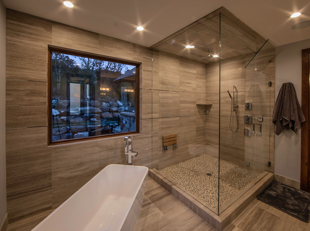 This is an example of a large contemporary ensuite bathroom in Denver with a console sink, shaker cabinets, dark wood cabinets, a freestanding bath, a corner shower, a two-piece toilet, grey tiles, stone tiles, grey walls and travertine flooring.