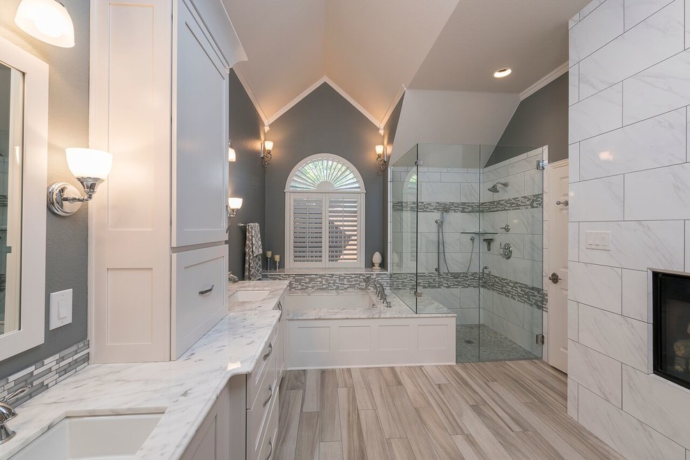 Inredning av ett klassiskt stort en-suite badrum, med skåp i shakerstil, vita skåp, ett undermonterat badkar, en kantlös dusch, grå kakel, marmorkakel, grå väggar, ljust trägolv, ett undermonterad handfat, marmorbänkskiva, brunt golv och dusch med gångjärnsdörr