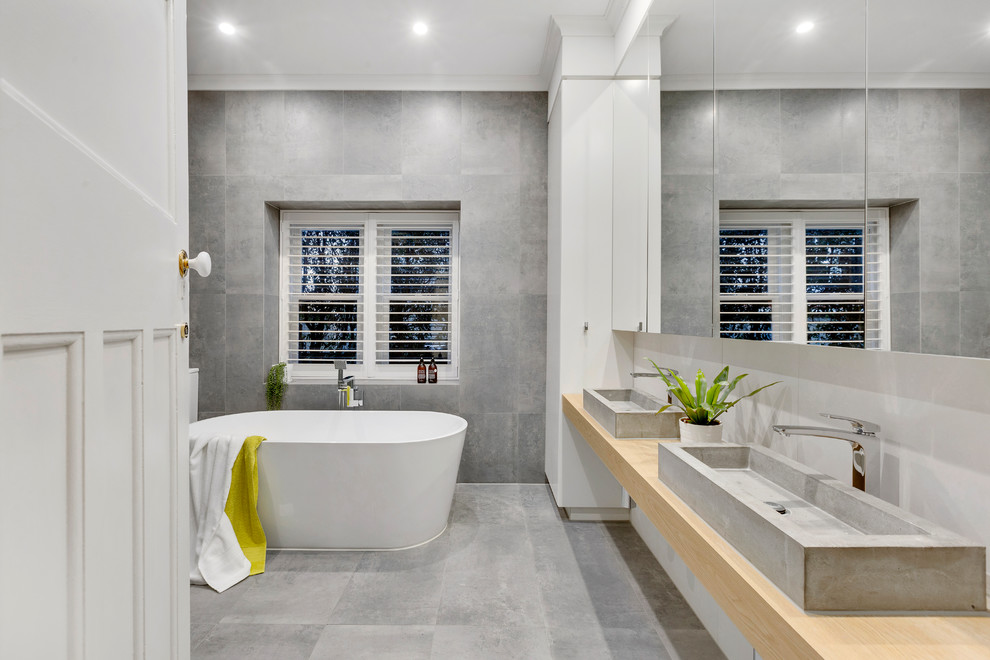 Example of a large minimalist master gray tile gray floor freestanding bathtub design in Melbourne with glass-front cabinets, gray walls, wood countertops and a vessel sink