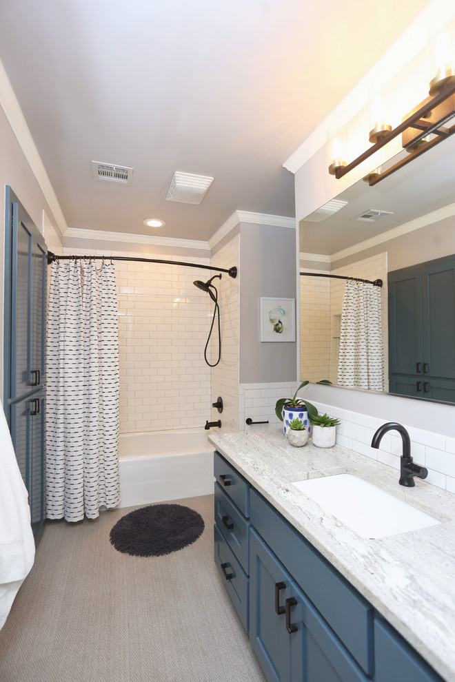 他の地域にあるトランジショナルスタイルのおしゃれなバスルーム (浴槽なし) (落し込みパネル扉のキャビネット、青いキャビネット、アルコーブ型浴槽、シャワー付き浴槽	、白いタイル、サブウェイタイル、グレーの壁、アンダーカウンター洗面器、ベージュの床、シャワーカーテン、ベージュのカウンター) の写真