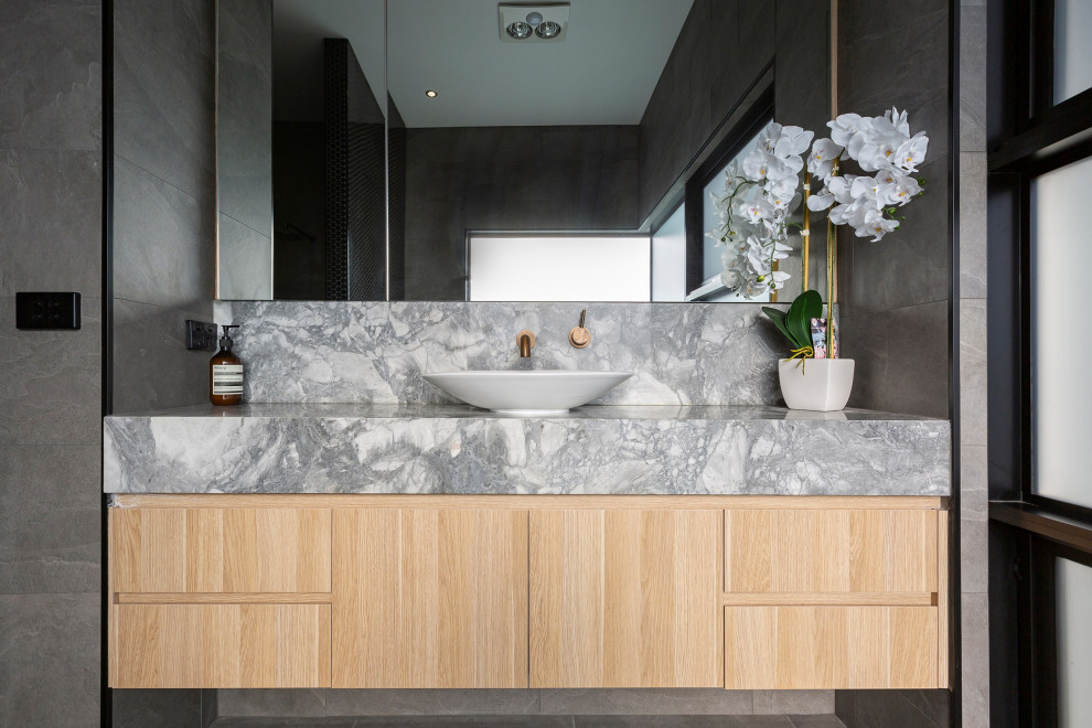 Foto på ett funkis grå en-suite badrum, med släta luckor, skåp i mellenmörkt trä, grå kakel, ett fristående handfat, marmorbänkskiva och grått golv