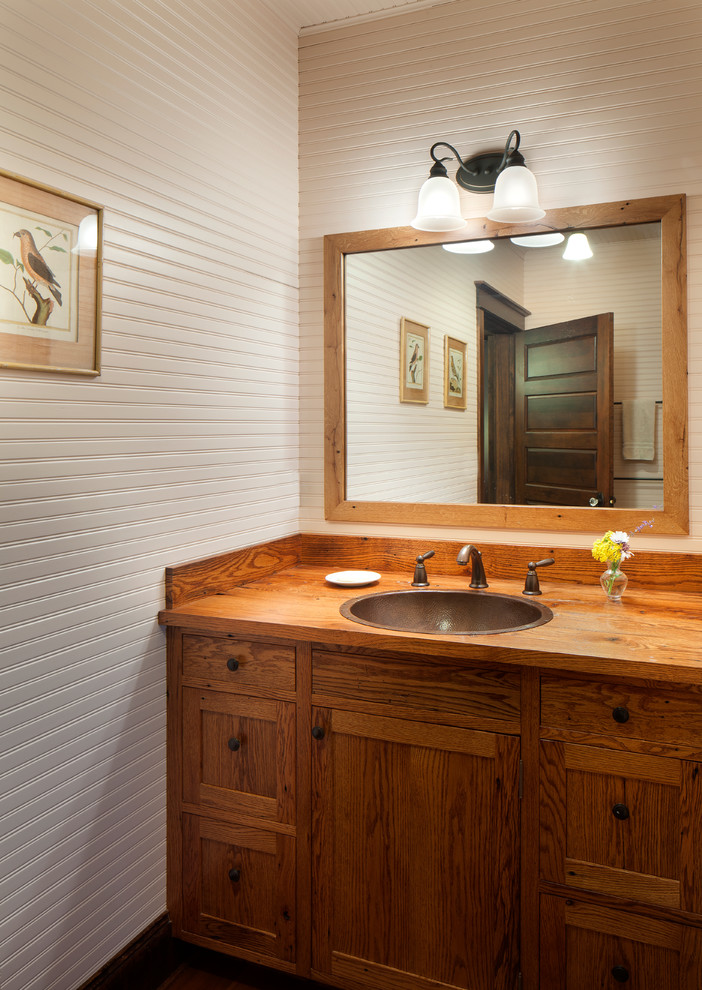 Modelo de cuarto de baño rústico con armarios estilo shaker, puertas de armario de madera oscura, paredes blancas, lavabo encastrado y encimera de madera