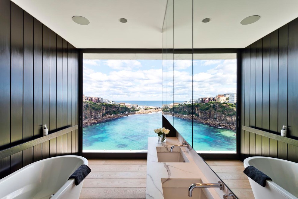 Trendy master light wood floor freestanding bathtub photo in Sydney with black walls, an undermount sink and marble countertops