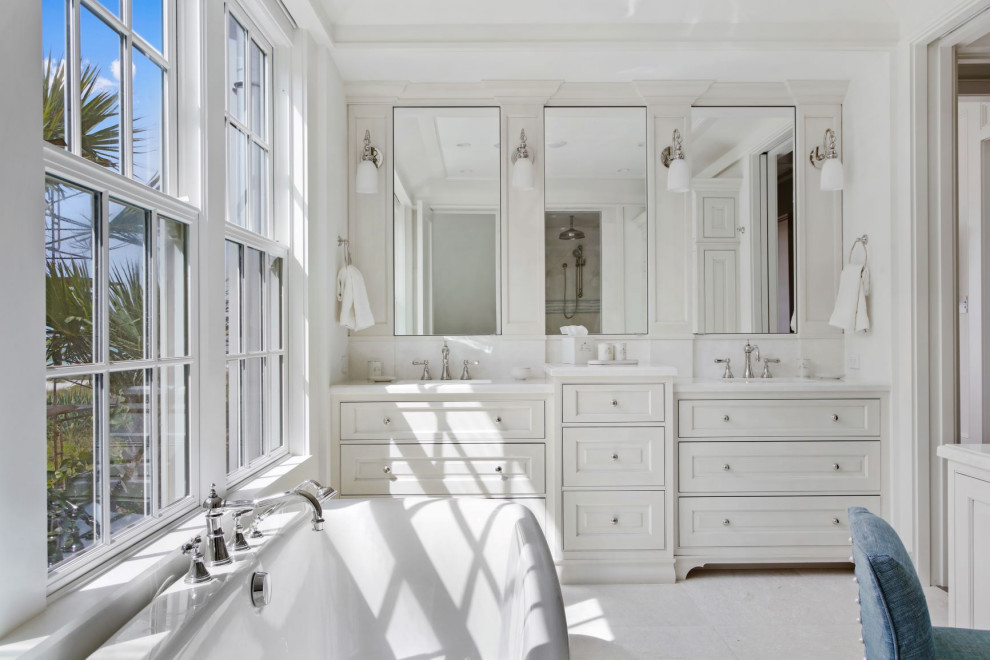 Aménagement d'une salle de bain principale bord de mer de taille moyenne avec des portes de placard blanches, une baignoire indépendante, un mur blanc, un sol en marbre, un lavabo encastré, un plan de toilette en quartz modifié, un sol blanc, un plan de toilette blanc et un placard à porte affleurante.