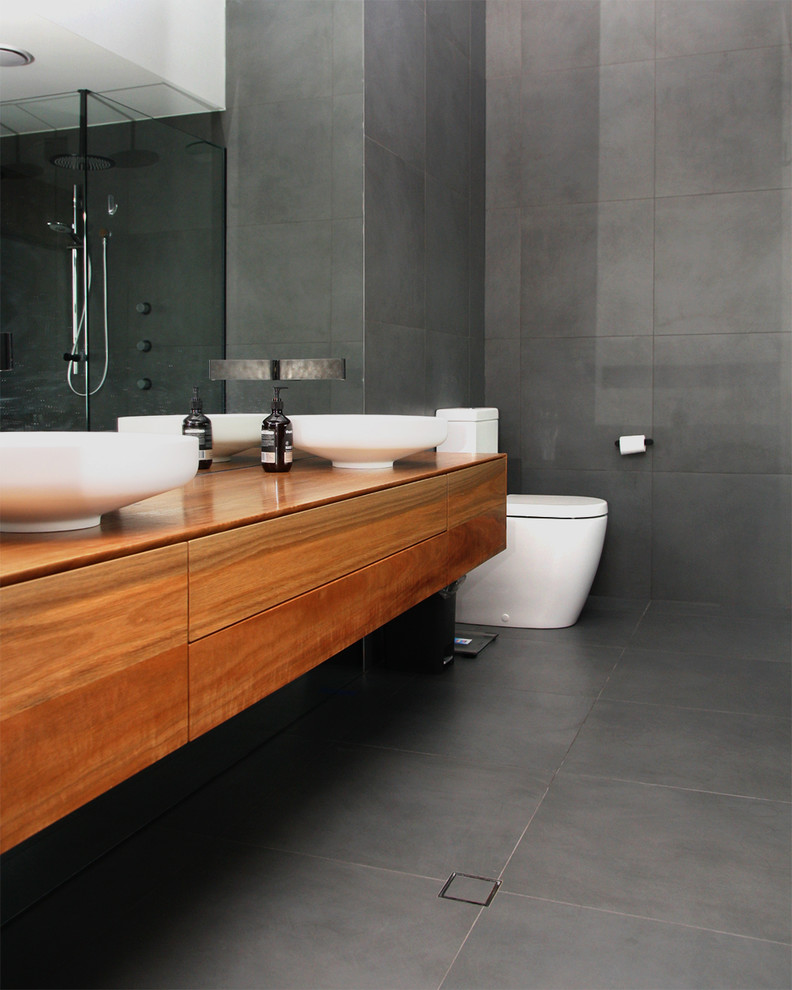 Inredning av ett modernt stort brun brunt en-suite badrum, med möbel-liknande, skåp i mellenmörkt trä, ett fristående badkar, en öppen dusch, en toalettstol med hel cisternkåpa, grå kakel, cementkakel, grå väggar, cementgolv, ett fristående handfat, träbänkskiva, grått golv och med dusch som är öppen