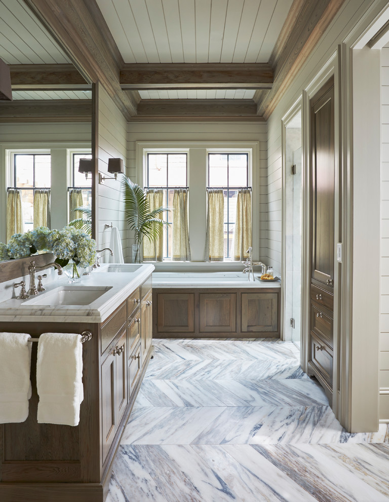 Aménagement d'une salle de bain bord de mer en bois brun avec un placard avec porte à panneau encastré, une baignoire encastrée, un mur blanc, un lavabo encastré, un sol blanc et un plan de toilette blanc.