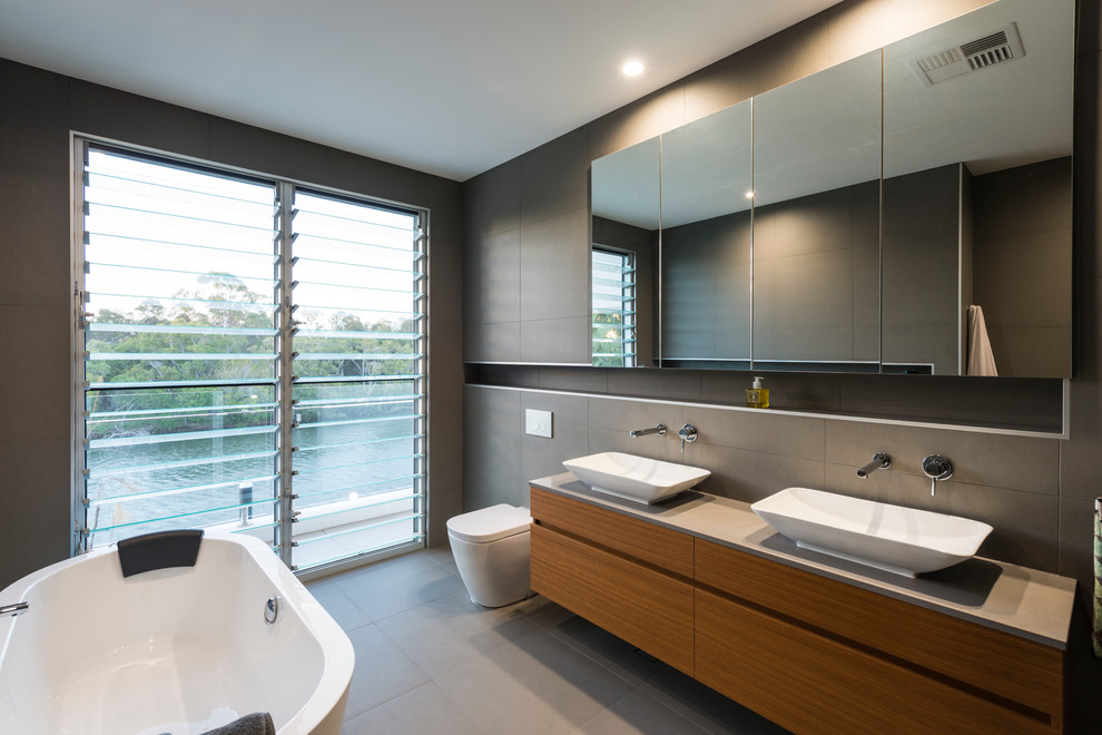 ゴールドコーストにあるコンテンポラリースタイルのおしゃれな浴室 (フラットパネル扉のキャビネット、中間色木目調キャビネット、置き型浴槽、一体型トイレ	、グレーのタイル、グレーの壁、ベッセル式洗面器) の写真