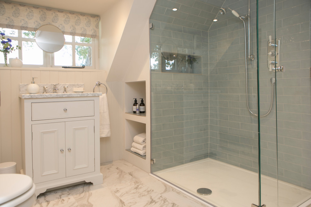 Idée de décoration pour une salle de bain principale champêtre avec un placard en trompe-l'oeil, des portes de placard grises, une baignoire indépendante, une douche ouverte, WC suspendus, un carrelage bleu, des carreaux de céramique, un mur beige, un sol en carrelage de céramique, un lavabo encastré, un plan de toilette en marbre, un sol gris, une cabine de douche à porte battante et un plan de toilette gris.