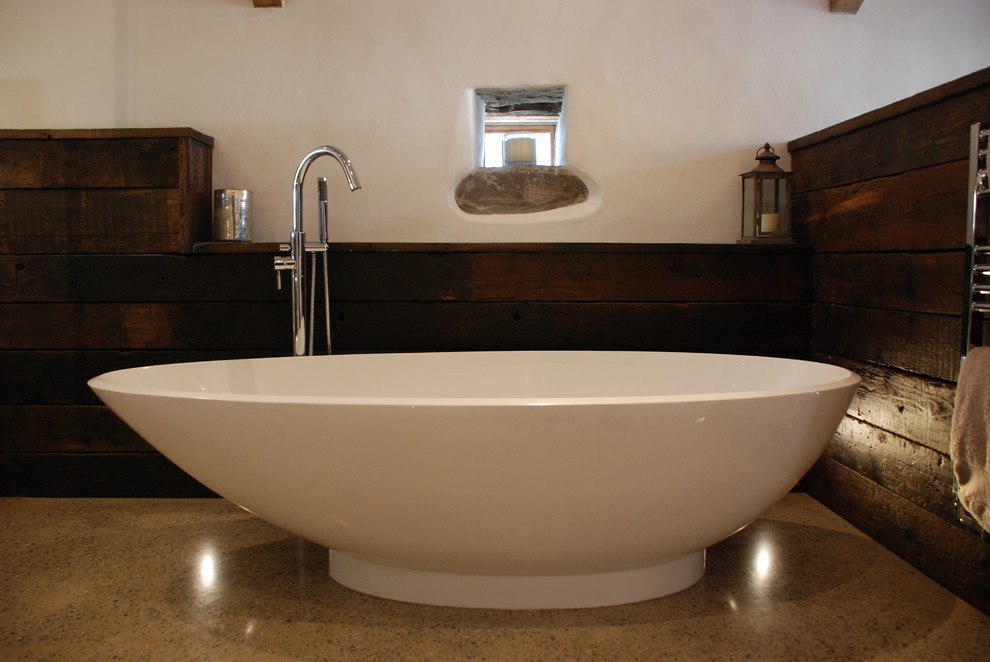 This is an example of an expansive contemporary ensuite bathroom in Cornwall with a wall-mounted sink, wooden worktops, a freestanding bath, a walk-in shower, a wall mounted toilet, white walls, concrete flooring, brown floors, a hinged door and exposed beams.