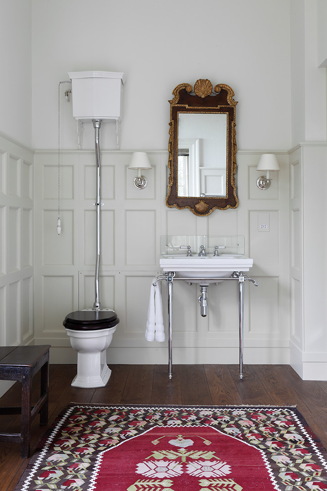 Imagen de cuarto de baño principal clásico con lavabo tipo consola, paredes blancas, suelo de madera oscura, sanitario de dos piezas y espejo con luz