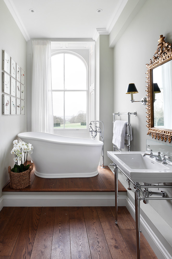 Inredning av ett klassiskt mellanstort en-suite badrum, med ett fristående badkar, grå väggar, ett konsol handfat och mörkt trägolv