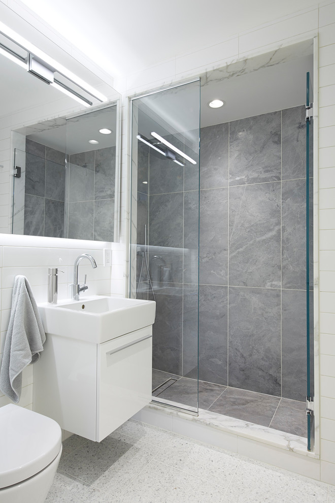 This is an example of a medium sized modern shower room bathroom in New York with flat-panel cabinets, white cabinets, an alcove shower, a wall mounted toilet, white tiles, ceramic tiles, blue walls, terrazzo flooring, a wall-mounted sink, white floors and a hinged door.