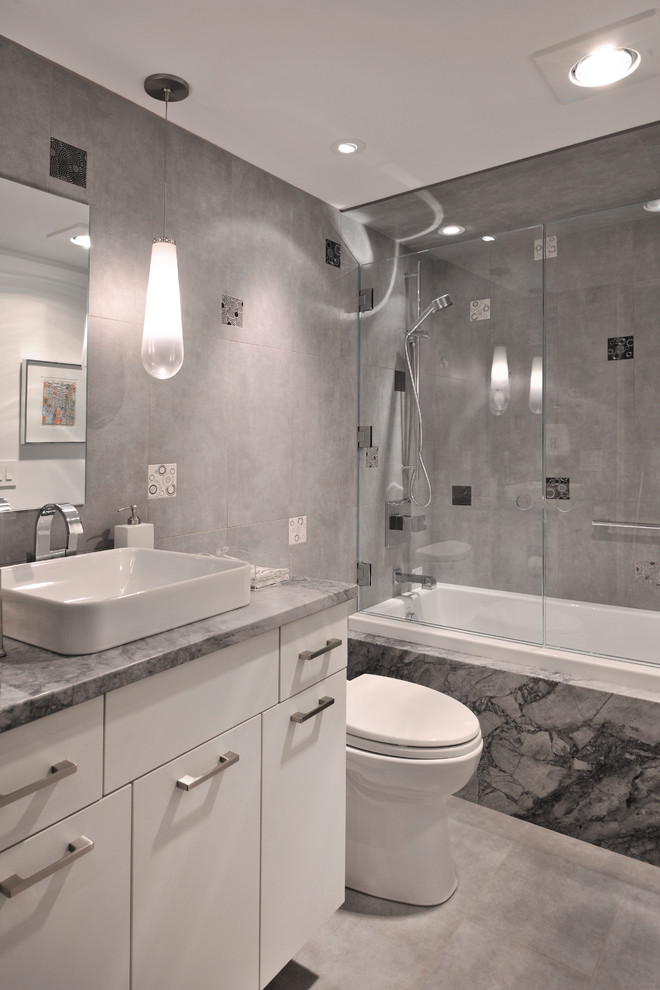 Idéer för ett modernt badrum med dusch, med ett fristående handfat, släta luckor, vita skåp, granitbänkskiva, ett platsbyggt badkar, en dusch/badkar-kombination, en toalettstol med hel cisternkåpa, grå kakel, porslinskakel, vita väggar och klinkergolv i porslin