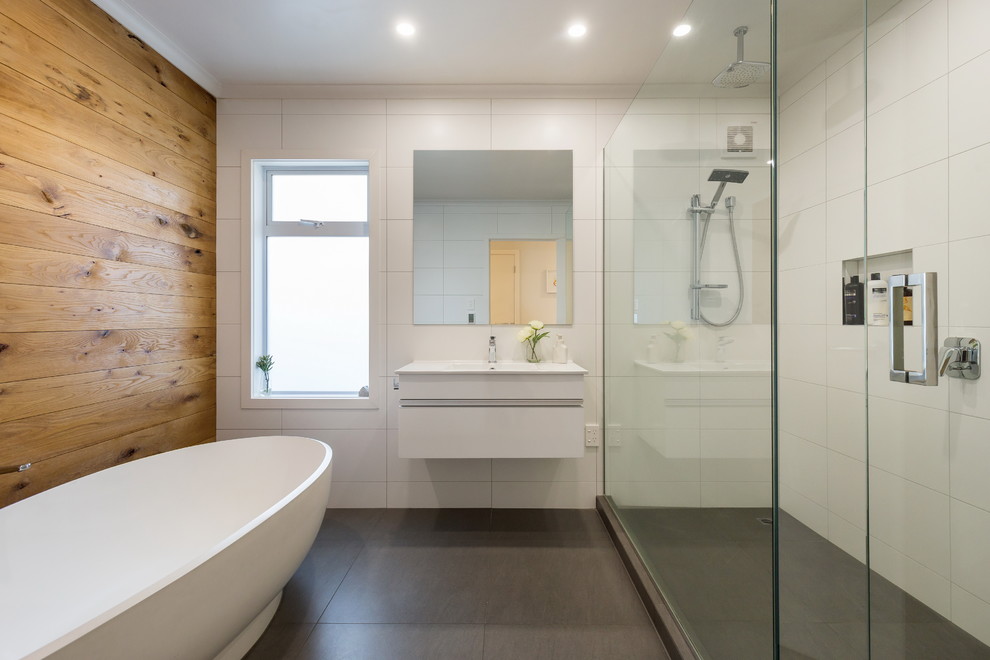 Modern inredning av ett mellanstort en-suite badrum, med vita skåp, ett fristående badkar, en dubbeldusch, en toalettstol med hel cisternkåpa, vit kakel, cementkakel, vita väggar, cementgolv, ett väggmonterat handfat, bänkskiva i täljsten, grått golv och dusch med gångjärnsdörr