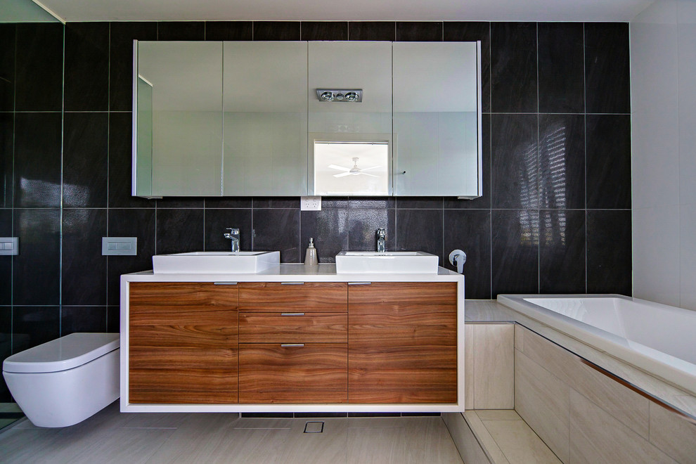 Aménagement d'une salle de bain principale moderne en bois brun avec un lavabo intégré, une baignoire posée, WC suspendus, un carrelage beige et un mur gris.