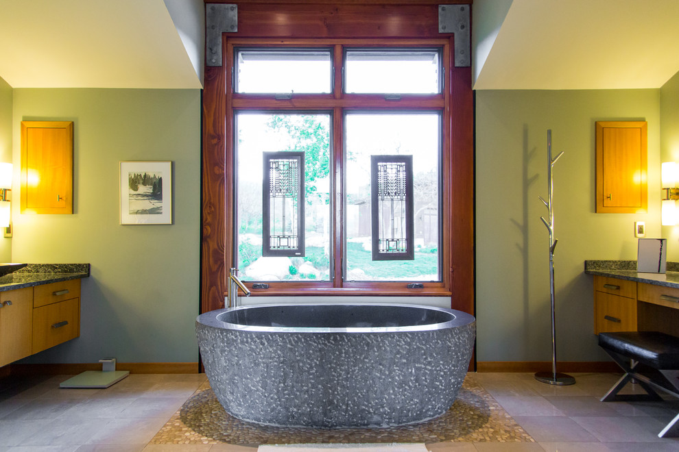 На фото: главная ванная комната в современном стиле с настольной раковиной, плоскими фасадами, светлыми деревянными фасадами, столешницей из гранита, отдельно стоящей ванной, зелеными стенами и мраморным полом