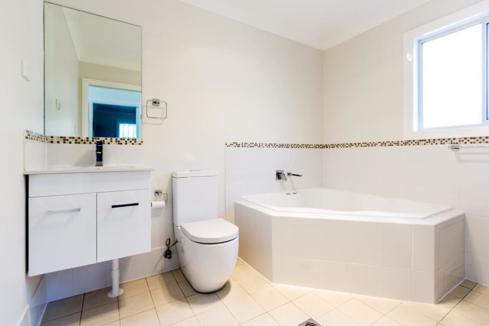 Example of a trendy master white tile and ceramic tile porcelain tile alcove shower design in Sydney with flat-panel cabinets, white cabinets, solid surface countertops, a hot tub, a one-piece toilet and white walls