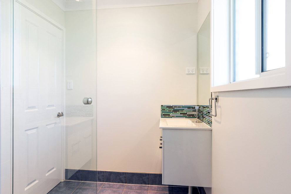 Example of a small trendy 3/4 multicolored tile and ceramic tile ceramic tile corner shower design in Sydney with a wall-mount sink, flat-panel cabinets, white cabinets, solid surface countertops, a one-piece toilet and white walls