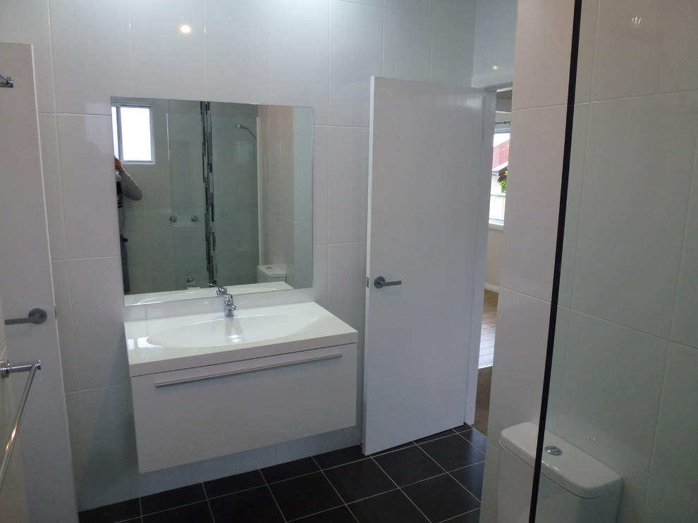 Cette image montre une petite salle de bain principale minimaliste avec un placard à porte plane, une douche d'angle, WC à poser, un carrelage blanc, des carreaux de céramique, un lavabo posé et un plan de toilette en surface solide.