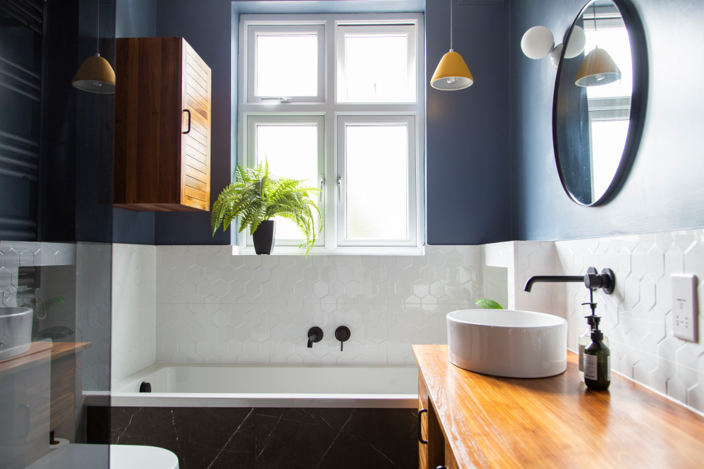 На фото: маленькая главная ванная комната в стиле неоклассика (современная классика) с коричневыми фасадами, накладной ванной, душевой комнатой, инсталляцией, белой плиткой, керамогранитной плиткой, синими стенами, полом из керамогранита, столешницей из дерева, черным полом, коричневой столешницей, тумбой под одну раковину, напольной тумбой, деревянным потолком и плоскими фасадами для на участке и в саду