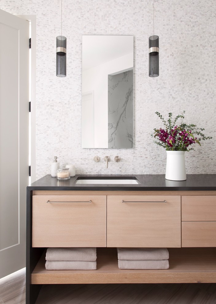 Modern inredning av ett badrum, med släta luckor, skåp i ljust trä, grå kakel, vit kakel, mosaik, flerfärgade väggar, laminatgolv, ett undermonterad handfat och bänkskiva i akrylsten