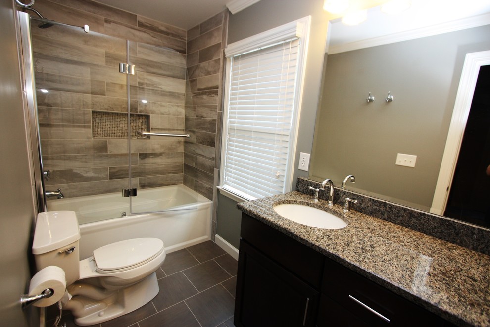 Medium sized contemporary bathroom in Raleigh with a submerged sink, recessed-panel cabinets, dark wood cabinets, granite worktops, an alcove bath, an alcove shower, a one-piece toilet, grey tiles, porcelain tiles, grey walls and porcelain flooring.