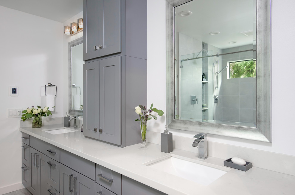 Inspiration for a large traditional ensuite bathroom in Seattle with flat-panel cabinets, grey cabinets, a freestanding bath, a walk-in shower, a one-piece toilet, white tiles, stone slabs, blue walls, light hardwood flooring, a built-in sink and solid surface worktops.