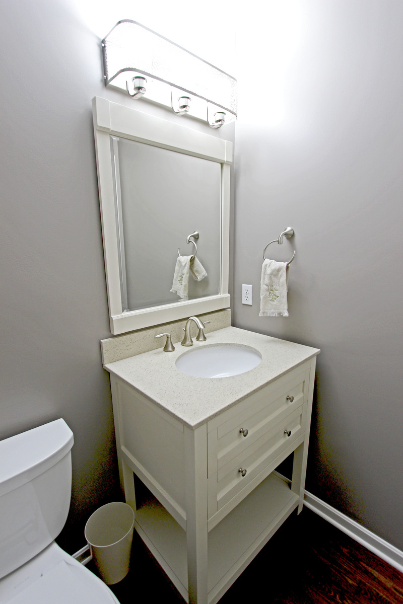 Inredning av ett klassiskt litet badrum med dusch, med möbel-liknande, vita skåp, en toalettstol med separat cisternkåpa, grå kakel, grå väggar, mörkt trägolv, ett undermonterad handfat, bänkskiva i kvarts och brunt golv