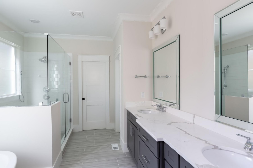 Пример оригинального дизайна: главная ванная комната среднего размера в классическом стиле с фасадами в стиле шейкер, серыми фасадами, отдельно стоящей ванной, угловым душем, раздельным унитазом, белой плиткой, керамической плиткой, белыми стенами, полом из керамической плитки, врезной раковиной, столешницей из искусственного кварца, серым полом, душем с распашными дверями и белой столешницей