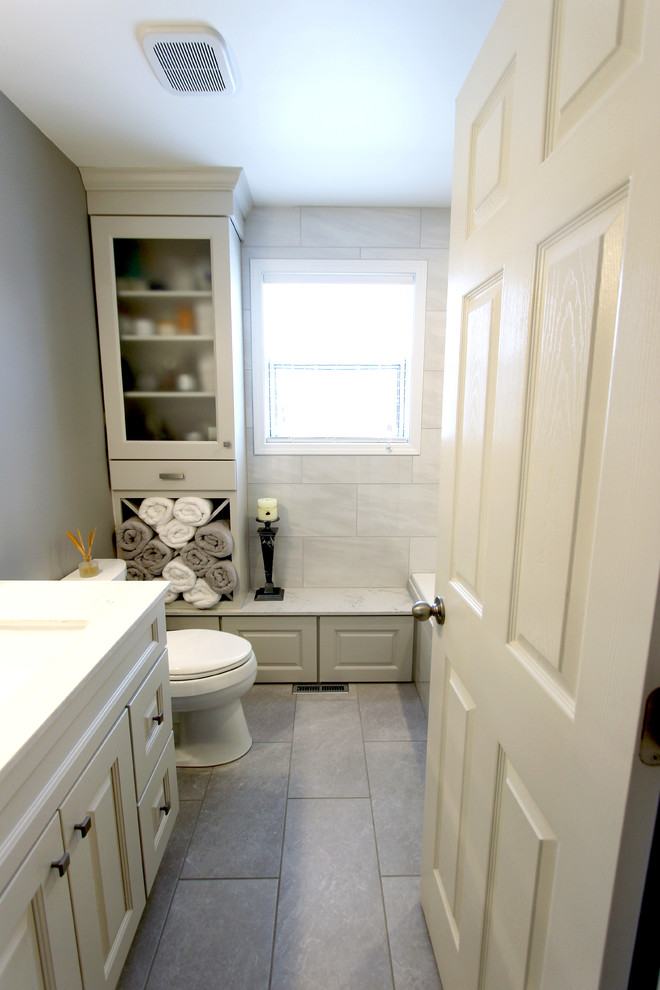 Inspiration for a small traditional ensuite bathroom in Cleveland with raised-panel cabinets, grey cabinets, an alcove bath, an alcove shower, a two-piece toilet, grey tiles, porcelain tiles, grey walls, porcelain flooring, a submerged sink, solid surface worktops, grey floors and a hinged door.