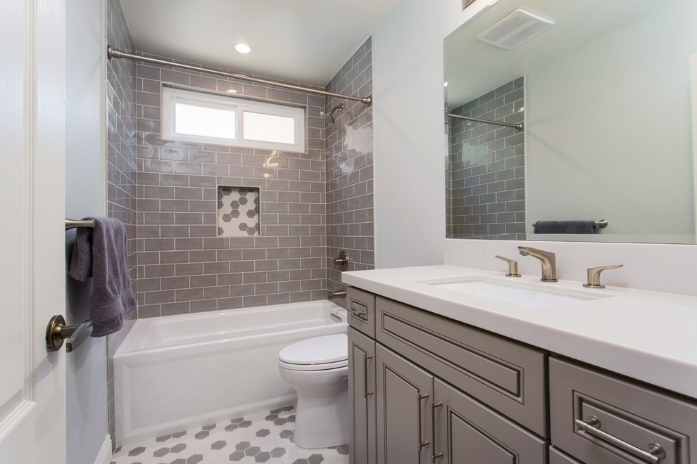 Cette image montre une petite salle d'eau traditionnelle avec un placard avec porte à panneau surélevé, des portes de placard grises, une baignoire en alcôve, un combiné douche/baignoire, WC à poser, un carrelage gris, un carrelage métro, un mur gris, un sol en carrelage de terre cuite, un lavabo encastré, un plan de toilette en quartz modifié, un sol gris et une cabine de douche avec un rideau.