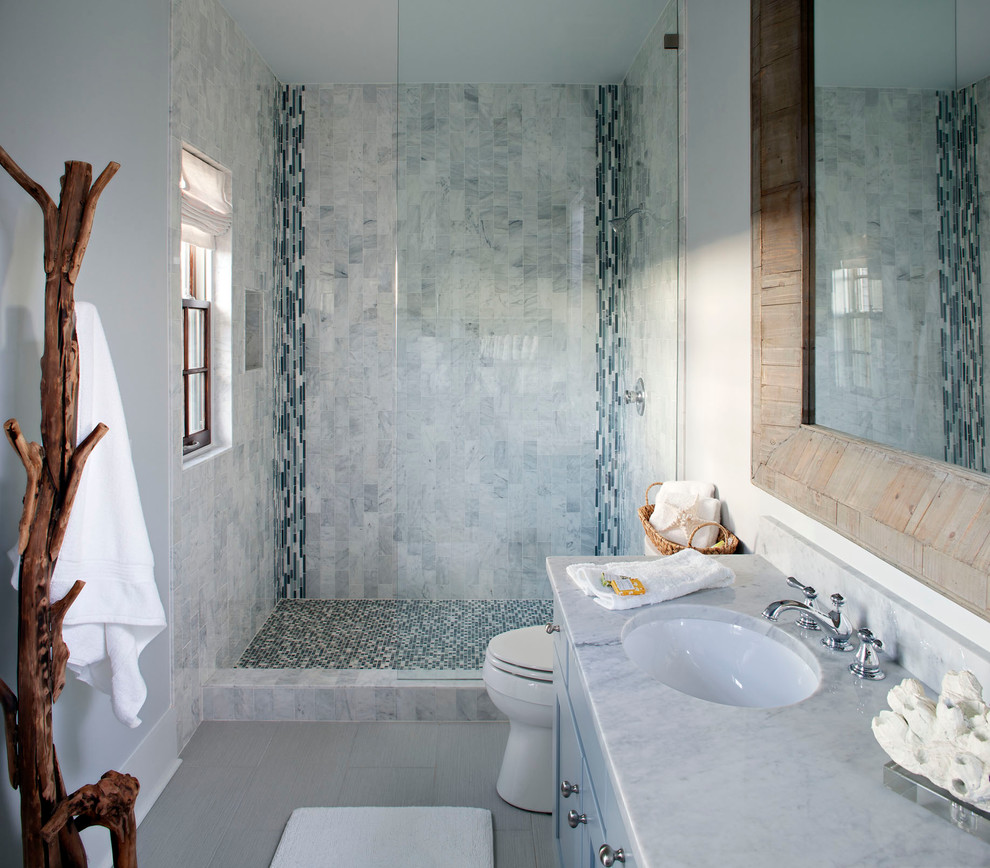 Modelo de cuarto de baño marinero con lavabo bajoencimera, puertas de armario azules, encimera de mármol, ducha empotrada y baldosas y/o azulejos en mosaico