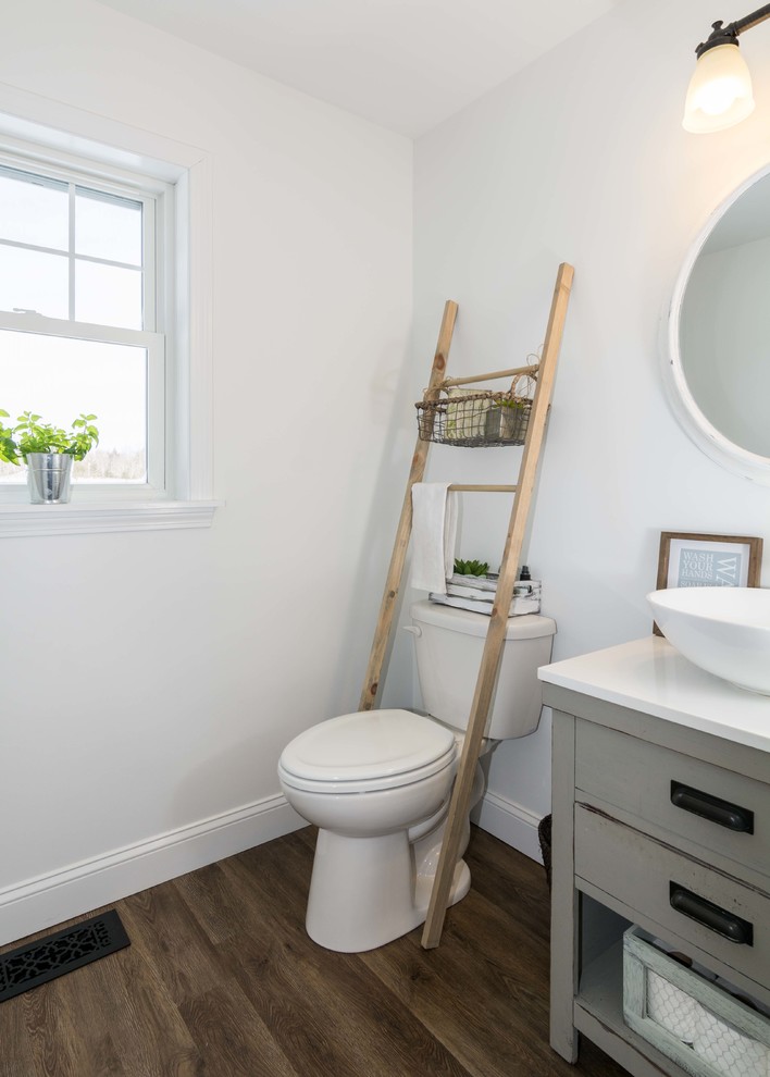 Bild på ett litet lantligt badrum med dusch, med möbel-liknande, grå skåp, vita väggar, vinylgolv, ett fristående handfat, en toalettstol med separat cisternkåpa, bänkskiva i akrylsten och brunt golv