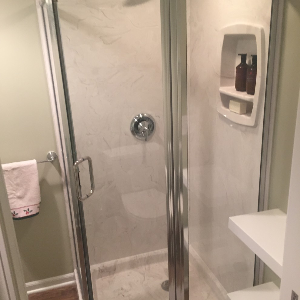 Cette image montre une petite salle d'eau traditionnelle avec une douche d'angle, un mur vert, un sol en vinyl, un lavabo suspendu et un plan de toilette en verre.