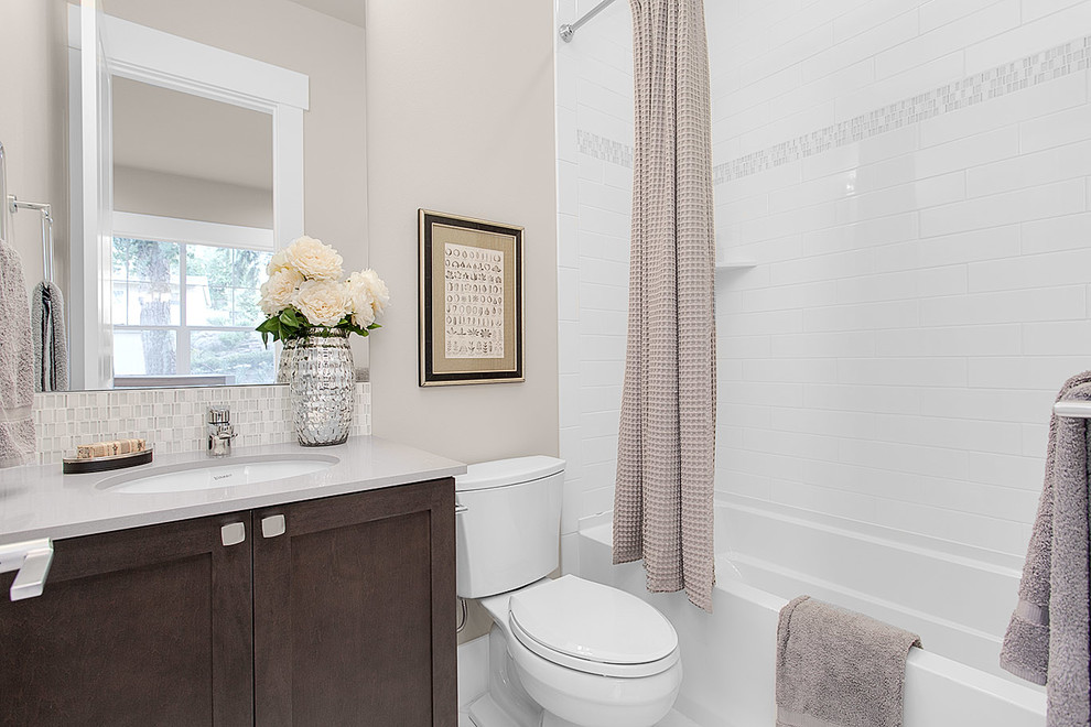 Design ideas for a medium sized traditional bathroom in Seattle with recessed-panel cabinets, dark wood cabinets, a shower/bath combination, a two-piece toilet, grey tiles, glass tiles, grey walls, a submerged sink and engineered stone worktops.
