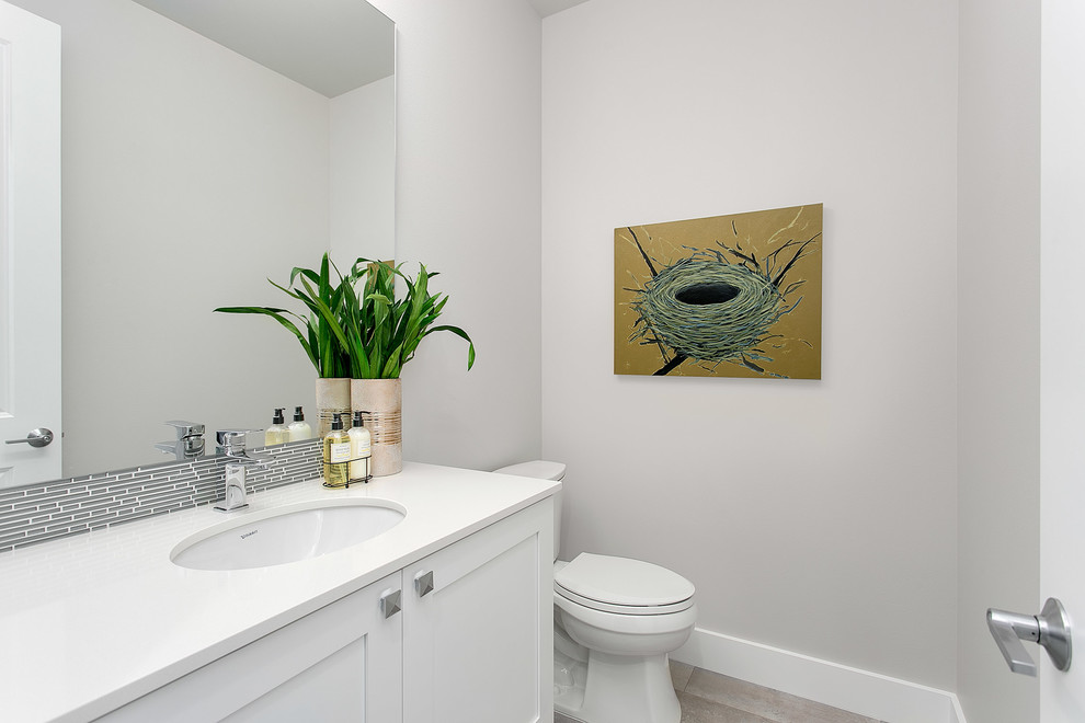 Cette photo montre une salle de bain chic de taille moyenne avec un placard à porte shaker, des portes de placard blanches, WC séparés, un carrelage gris, un mur gris, un lavabo encastré et un plan de toilette en quartz modifié.